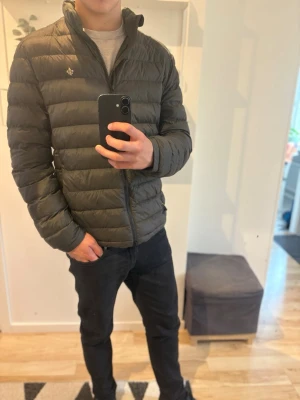  Morris jacka  - Säljer en olivgrön dunjacka från Morris med quiltad design och hög krage. Jackan har dragkedja framtill och en liten logga på bröstet. Perfekt för hösten och riktigt snygg till både jeans och sneakers. Storlek S men sitter som M