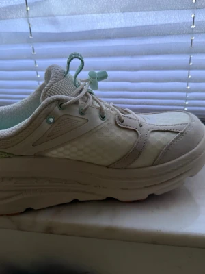 Vita hooka sneakers med mintdetaljer - Helt nya Hoka skor. Aldrig använda. Ångrat köp efter att ha gått med dem inomhus. vitt med mintgröna detaljer och snörning med snabblås. Ovandelen är i mesh och syntetmaterial med hexagonmönster på sidan. Tjock sula för extra komfort och trendig look. Stl 39. Men funkar för en 38. 