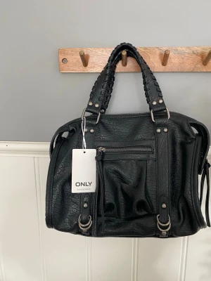 Svart handväska från ONLY - En helt ny och oanvänd väska med prislappen kvar. En bra skolväska som man får plats med det mesta i, den är svart med lite silver detaljer. Behöver du en väska med bra utrymme så skulle jag rekommendera denna, den är varken för liten eller för stor. Den är lagom stor och funkar till allt💕