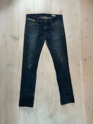 Mörkblå raka jeans med slitningar - Snygga mörkblå jeans med raka ben och diskreta slitningar. Klassisk femficksmodell med kopparfärgade nitar och knappstängning. Jeansen har en tidlös tvätt och passar perfekt till en avslappnad stil.