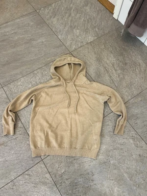 Kashmir hoodie  - Säljer en stilren beige hoodie med huva och dragsko. Hoodien har långa ärmar, ribbade muddar och är tillverkad i ett mjukt, stickat material. Perfekt för en avslappnad look och enkel att matcha med jeans eller mjukisbyxor.