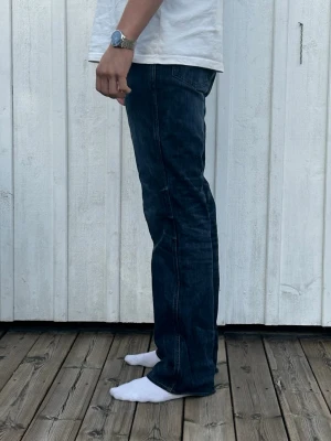 Mörkblå Wrangler WRANCHER - Säljer ett par mörkblå bootcut jeans med  en lätt tvättad look och raka ben som går ut något vid ankeln. OBS jeansen har blivit lagade vid sömmen baktill (bild 3)
