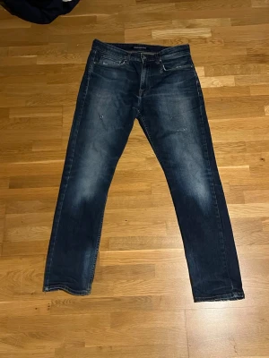 Mörkblå raka jeans - Snygga mörkblå jeans med raka ben och diskreta slitningar framtill. Klassisk femficksmodell med dragkedja och knapp. Jeansen har en midja på cirka 40 cm enligt bild. Perfekta för en avslappnad och trendig stil.