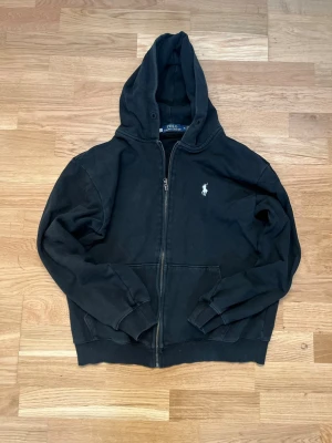 Svart Ralph Lauren Zip - Tröja - En skön svart Ralph Lauren Tröja med vit emblem. Passar till dig som vill hålla värmen utan att förlora stilen. Perfekt nu till Höst och Skolstart. 