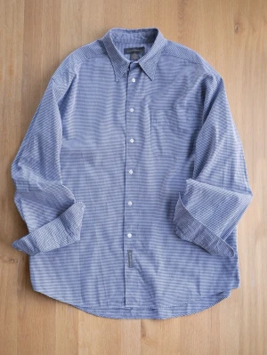 Vintage Blårutig skjorta från Banana Republic - Klassisk blårutig skjorta från Banana Republic med vit knappstängning och bröstficka. Skjortan har lång ärm och en avslappnad passform, perfekt för en stilren look. Tillverkad i mjuk bomull som känns skön mot huden.
