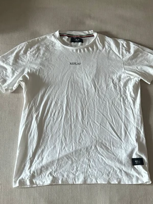 Vit t-shirt från Replay - Klassisk vit t-shirt från Replay med rund hals och korta ärmar. Diskret Replay-logga broderad på bröstet och en liten etikett nere vid fållen. Tillverkad i mjuk bomull för en skön känsla.