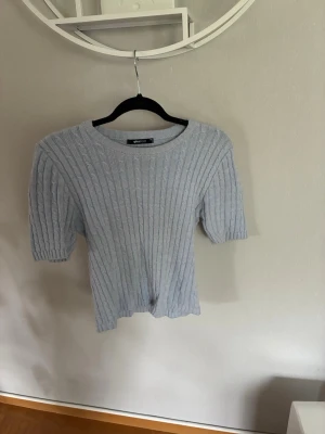 Ljusblå ribbstickad topp - Säljer en ljusblå ribbstickad topp med korta ärmar och rund halsringning. Tröjan har en smal passform och är perfekt för dig som gillar en enkel men stilren look. Materialet känns mjukt och bekvämt mot huden.