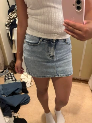 Ljusblå jeanskjol i kort modell - Trendig ljusblå jeanskjol i kort modell med klassiska fem fickor och dragkedja framtill. Kjolen har en normal passform och är perfekt för en avslappnad och cool stil. Passar till både sneakers och boots.