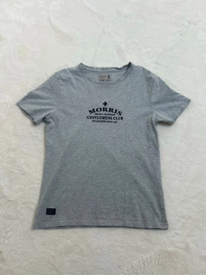 Grå t-shirt från Morris - Snygg grå t-shirt från Morris med tryck på bröstet där det står 'Morris Gentlemens Club'. Klassisk passform och rund halsringning. Perfekt till jeans eller shorts för en avslappnad stil.