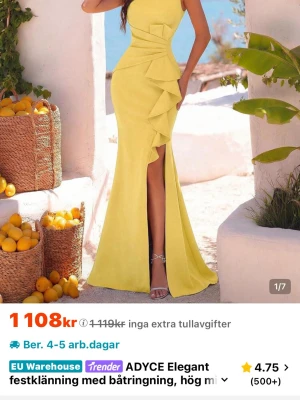 Gul långklänning med volang och slits - Elegant gul långklänning med figurnära passform, volangdetaljer längs sidan och hög slits framtill. Klänningen har ärmlös design och öppen rygg, perfekt för sommarens och festliga  speciella tillfällen. Tillverkad i ett mjukt, följsamt material som ger en lyxig känsla.