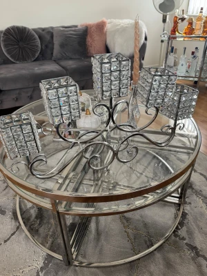 Lyxig ljusstake i silver och glas - Säljer en elegant ljusstake i silverfärgad metall med fem hållare dekorerade med fyrkantiga glaskristaller. Ljusstaken har en modern design med snirkliga detaljer och passar perfekt som centerpiece på soffbordet eller matbordet. Original priset på denna låg på 850kr. 
