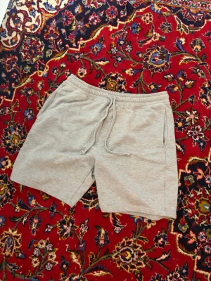 Grå sweatshorts från Pull&Bear - Säljer ett par ljusgrå sweatshorts från Pull&Bear med snörning i midjan och två sidofickor. Perfekta för chill dagar eller träning. Mjukt material i bomull och elastisk midja för extra komfort.