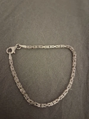 Silverarmband i kedjemodell 925 - Snyggt armband i äkta silver (925) med en detaljerad kedjedesign. Armbandet har en klassisk karbinlås och en stilren, flätad struktur som ger en modern touch. Perfekt accessoar för att lyfta din outfit.