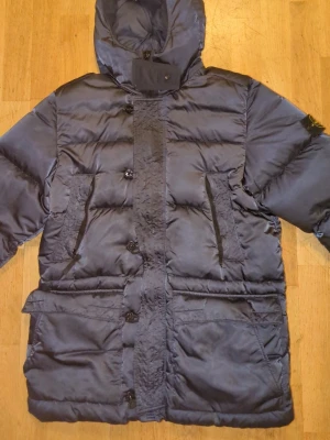 Stone Island Vinterjacka - Snygg mörkblå dunjacka från Stone Island.. Jackan har en klassisk patch på ärmen, dragkedja och knappar framtill samt förstärkta partier på armbågarna. Perfekt för kalla vinterdagar och riktigt street. Pris kan diskuteras vid snabb affär.