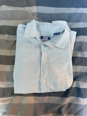 Linne skjorta från Jack & Jones - Snygg ljusblå skjorta från Jack & Jones med klassisk krage och knäppning framtill. Tillverkad i ett lätt och svalt material, perfekt för varmare dagar. Enkel och stilren design som passar till många olika outfits.