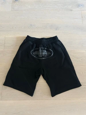 Corteiz shorts - Svarta shorts med elastisk midja och ett ovalt tryck framtill. Modellen är loose fit och har en bakficka. Perfekta för en avslappnad stil under varmare dagar.