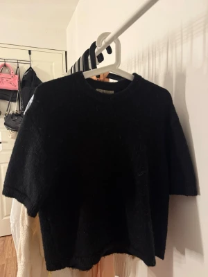 Svart stickad tröja Gina Tricot - Svart stickad tröja från Gina Tricot med korta ärmar och rund hals. Tröjan är i ett mjukt, fluffigt material och har en enkel, oversized passform. OBS ⚠️⚠️ Har haft ett hål baktill som sytts igen, men inget som märks av vid användning! 