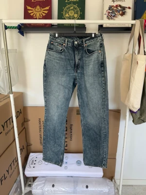Blå raka jeans med hög midja - Säljer ett par blå tvättade jeans med rak passform och hög midja. Jeansen har klassiska fem fickor, bälteshällor och knappgylf. Materialet är kraftigt denim i bomull och färgen är en snygg mellanblå tvätt.