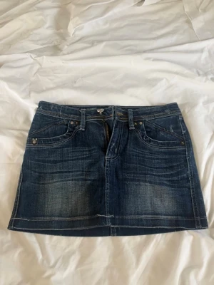 Mörkblå jeanskjol med dragkedjor - Snygg mörkblå jeanskjol i klassisk modell med slitna detaljer. Kjolen har dragkedjor på bakfickorna och en kort passform som ger en cool och avslappnad vibe🤩🙌