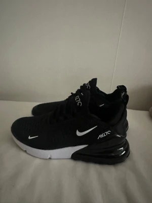 Nike Air Max 270  - Svarta Nike Air Max 270 sneakers med vit sula och vita detaljer. Skorna har en luftig mesh-överdel, tydlig Air Max-dämpning i hälen och klassisk Nike-logga på sidan och tungan. Snygg och sportig design som passar till streetwear. Använd 1 gång