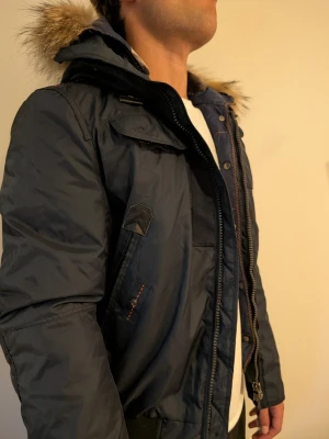 Parajumpers Masterpiece parka, marinblå, stl S - Parajumpers-parkas ur "Masterpiece Series", marinblå med pälskantad luva. Stl S. Använd men i gott skick, inga skador eller fläckar som jag kan hitta. Ett riktigt tekniskt plagg, håller vad den lovar när det är kallt ute. Modell: 182cm | 83kg.