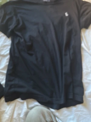 Svart t-shirt från Polo Ralph Lauren - Klassisk svart t-shirt från Polo Ralph Lauren med liten broderad logga på bröstet. T-shirten har rund hals och korta ärmar, perfekt till alla dina outfits. Tillverkad i mjuk bomull för skön känsla hela dagen.