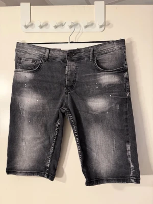 Grå jeansshorts från Dsquared2 - Säljer ett par grå jeansshorts från Dsquared2 med slitna detaljer och coola blekta partier. Klassisk femficksmodell med knappgylf och normal passform. Perfekta för en avslappnad streetstyle-look.