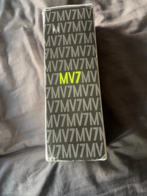 MV7 Mikrofon i originalkartong - Säljer en MV7 mikrofon i sin originalkartong. Kartongen är svart med grå text och har tydlig märkning 'MV7' i gult. Perfekt för podd, streaming eller inspelning. Mikrofonen är känd för sin höga ljudkvalitet och passar både till dator och annan ljudutrustning.
