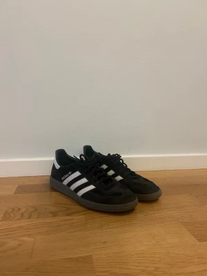 Adidas svartvita specizial sneakers - Säljer ett par klassiska Adidas sneakers i svart mocka med vita detaljer och de ikoniska tre ränderna på sidan. Skorna har lågt skaft och gummisula. Perfekta för en stilren och sportig look.