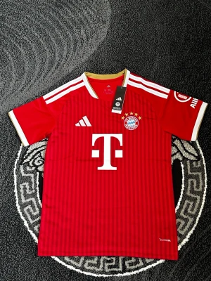 Röd Bayern München matchtröja - Säljer en röd Bayern München matchtröja från Adidas med vita och guldiga detaljer. Tröjan har klubbmärke och sponsortryck på bröstet samt tre stjärnor ovanför loggan. Tillverkad i funktionsmaterial som passar perfekt till fotbollsträning.