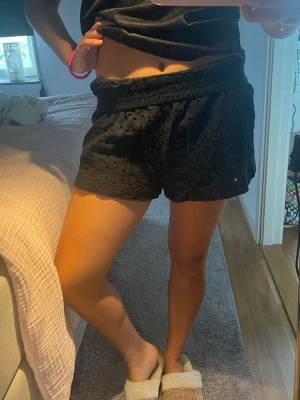 Svarta beach shorts med hålmönster - Snygga svarta shorts med hålmönster och broderade detaljer. De har elastisk midja och en avslappnad passform som ger en chill vibe. Perfekta för varma dagar och enkla att matcha med olika toppar.