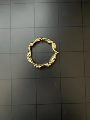 Guldigt armband med pärldetaljer - Snyggt armband i guldfärgad metall med unika, vridna pärlliknande delar och små runda pärlor mellan varje sektion. Armbandet har en modern och cool design som sticker ut och passar perfekt till din stil.