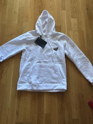 Vit hoodie från Prada med huva - Snygg vit hoodie från Prada med klassisk huva och känguruficka framtill. Hoodien har en diskret Prada-logga på bröstet och är tillverkad i mjukt material som känns skönt mot huden. Perfekt för dig som vill ha en clean och exklusiv look.