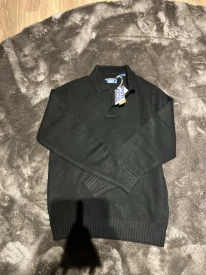 Svart stickad tröja från Jack & Jones - Snygg svart stickad tröja från Jack & Jones med klassisk krage och ribbade muddar. Perfekt till vardags eller när du vill vara lite extra uppklädd. Tröjan har en stilren look och är tillverkad i mjukt material för skön komfort.