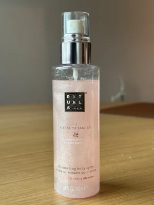 Rituals The Ritual of Sakura Body Spray - Shimmering body spray från Rituals, The Ritual of Sakura. Innehåller ris-mjölk och körsbärsblomma. Kommer i en genomskinlig flaska med rosa, skimrande vätska och silvrig spraypump. Ger huden en lätt doft och glow.
