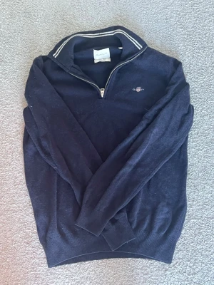 Gant half zip tröja - Svart långärmad tröja från gant med halv dragkedja och vit randdetalj på kragen. Tröjan har en liten broderad logga på bröstet och ribbade muddar vid ärmslut och nederkant. Perfekt för en stilren och avslappnad look. Knappast använd väldigt bra skick! Säljer för 300 kan med på priser ner till 200
