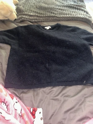 Svart stickad tröja Gina Tricot - Mysig svart stickad tröja från Gina Tricot i storlek 158/164. Tröjan har en enkel, rak passform med rund halsringning och kortare ärmar. Perfekt att matcha med jeans eller kjol för en avslappnad look.