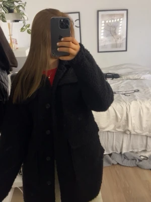 Svart teddy-cardigan med fickor - Mysig svart cardiganjacka i teddy-material med stora knappar framtill och två rejäla fickor. Jackan har en avslappnad passform och klassisk krage. Jag är 165 och den går över rumpan och låren💕