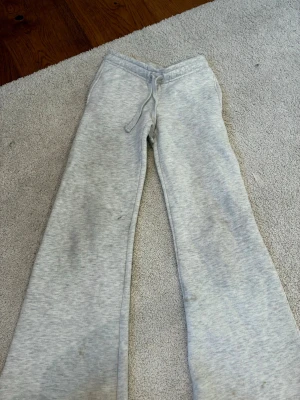 Grå mjukisbyxor med raka ben - Ett par ljusgrå mjukisbyxor med raka ben och dragsko i midjan. Byxorna har två bakfickor med broderad detalj och är tillverkade i mjukt sweatshirtmaterial. Perfekta för en avslappnad och chill stil.