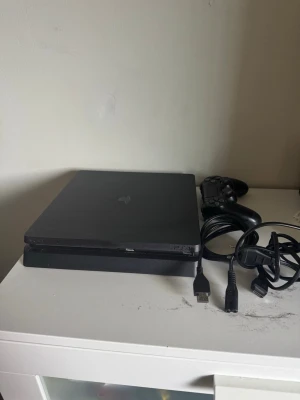 PlayStation 4 Slim spelkonsol svart - Säljer en svart PlayStation 4 Slim från Sony. Konsolen har en stilren, platt design och är tillverkad i matt plast. Medföljer gör en svart handkontroll samt strömkabel och hdmi kabel. Perfekt för gaming och streaming.