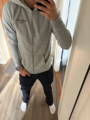 Ljusgrå zip hoodie Björn Borg - Snygg ljusgrå hoodie från Björn Borg med dragkedja framtill och två fickor. Klassisk huva och diskret logga på bröstet. Tillverkad i mjukt material som passar perfekt till en avslappnad stil.