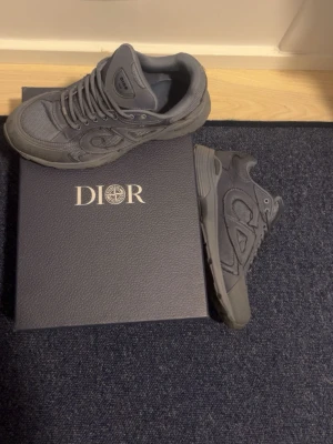 Grå Dior sneakers i mesh och mocka - Snygga grå sneakers från Dior med en chunky sula och detaljer i både mesh och mocka. Skorna har klassisk snörning och diskreta Dior-loggor på sidan och plösen. Perfekta för dig som gillar exklusiva och stilrena sneakers.  Pris kan snackas om tycker inte om de. 