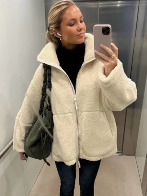 H&M trendig höst fleece jacka  - Säljer en krämvit teddyjacka med dragkedja framtill och stora fickor. Jackan har hög krage och en oversized passform som ger en riktigt mysig vibe. Tillverkad i fluffigt teddy-material som håller dig varm under kalla dagar.