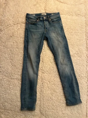 Blå slim fit jeans med slitningar - Snygga blå slim fit jeans med lätt slitna detaljer och klassisk femficksdesign. Jeansen har normal midja och smala ben, perfekta för en avslappnad och trendig look. Materialet är mjukt denim som ger en skön känsla hela dagen.
