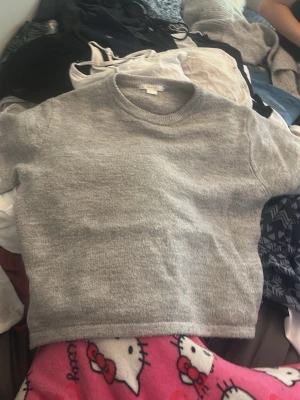 Grå stickad tröja från Gina Tricot - Mysig grå stickad tröja från Gina Tricot med rund halsringning och ribbade muddar vid ärmslut och nederkant. Enkel och stilren design som passar perfekt till jeans eller kjol. Materialet känns mjukt och behagligt mot huden.