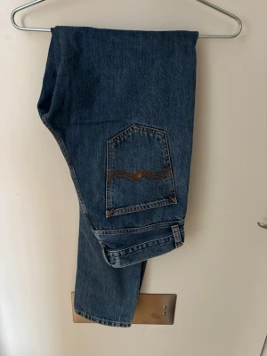 Blå raka jeans med broderad ficka - Säljer ett par klassiska blå jeans med rak passform och snygg broderad bakficka i orange. Jeansen har normal midja och är tillverkade i slitstark denim. Perfekta till vardags och passar till det mesta i garderoben. Storleken(bredd) 30 (längd) 34. Jag är 190