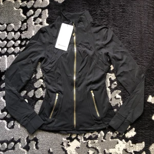 Lululemon Define Jacket Luon – Svart, storlek 2 - Helt ny med etiketter. Mjuk, stretchig och figurnära modell i Luon-material med guldfärgad dragkedja. Färg: Svart Storlek: 2 Helt ny med etiketter Hör av dig vid intresse!