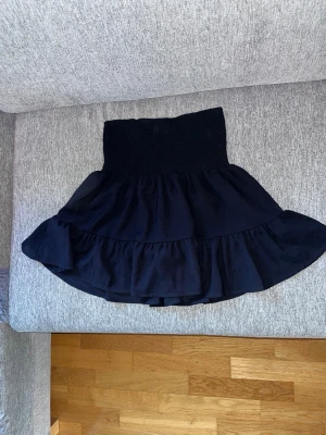 Svart volangskort med resårmidja - Supersöt svart skort med bred smockresår i midjan och dubbla volanger. Kjoldelen är i ett tunt, flowy tyg och shortsdelen undertill gör den både bekväm och praktisk. Perfekt för dig som vill ha kjolkänsla men ändå känna dig trygg. Passar till många olika stilar.
