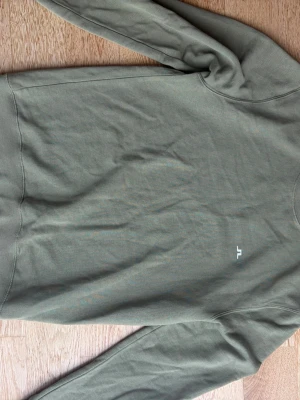 Olivgrön sweatshirt från J.Lindeberg - Snygg olivgrön sweatshirt från J.Lindeberg med rund halsringning och diskret vitt logotryck på bröstet. Tillverkad i mjuk bomull för en skön känsla. Perfekt till jeans eller joggers för en avslappnad look.