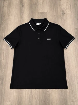 Svart pikétröja från BOSS - BOSS T-shirt 👕🔥  Säljer en snygg BOSS T-shirt i mycket bra skick. • Storlek: 14 - s • Märke: BOSS • Pris: 450 kr • Skick: Mycket bra skick  Stilren och snygg T-shirt som passar perfekt till jeans eller shorts. Packas noggrant och skickas snabbt 📦